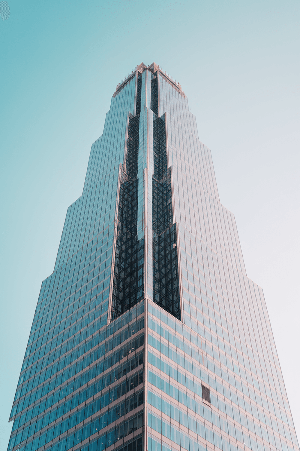 Glass-clad residential tower rising into a clear teal sky